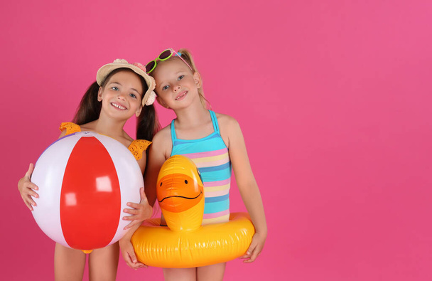 Cute little children in beachwear with bright inflatable toys on pink background. Space for text - Foto, afbeelding
