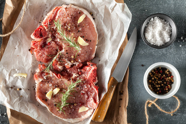 Two raw pork steaks grey stone background with rosemary and spices. Top view, copy space - Fotoğraf, Görsel