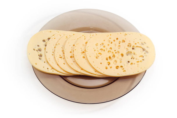 Large thin slices of the Swiss-type cheese with a lot of holes, so called the cheese's eyes on a dark glass dish on a white background - Photo, Image