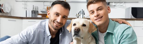 hombres homosexuales alegres sonriendo con el perro en casa, bandera - Foto, imagen