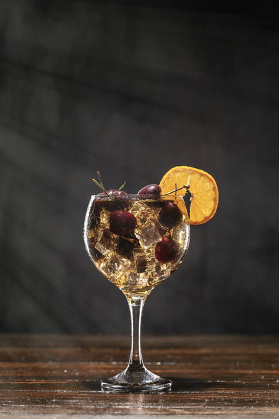Yellow cocktail with cherry in a glass standing on a wooden table, decorated with a slice of orange - Zdjęcie, obraz