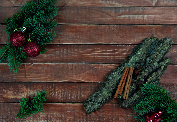 Des branches d'épinette avec des décorations de Noël rouges reposent sur une planche de bois marron avec un morceau d'écorce et un bâton de cannelle - Photo, image
