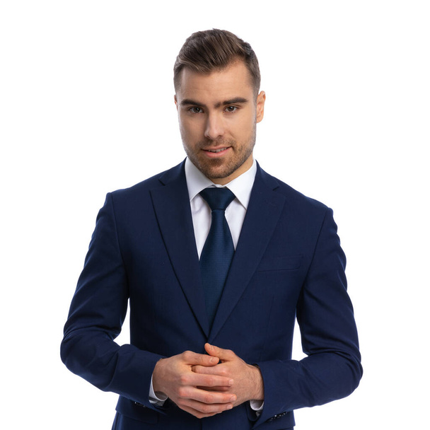 sexy elegant guy in navy blue suit smiling, touching fingers and posing, standing isolated on white background in studio, portrait - Zdjęcie, obraz