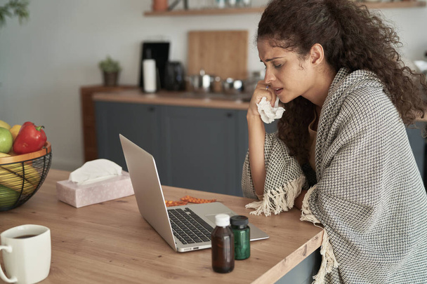 Kranke Frau sitzt zu Hause vor dem Laptop                                - Foto, Bild