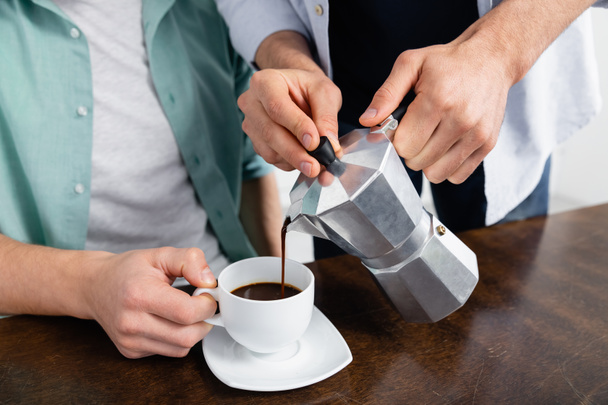 обрезанный вид гомосексуального мужчины, наливающего кофе в чашку рядом с мужем  - Фото, изображение
