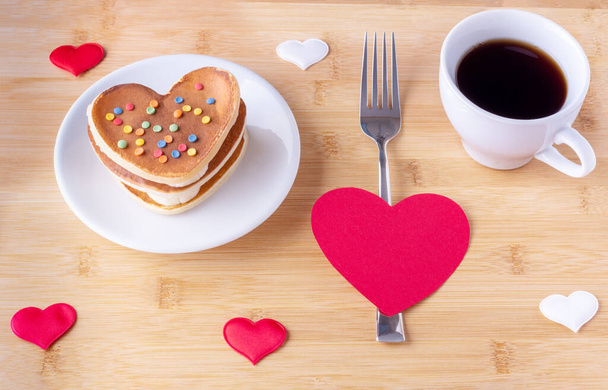 Homemade heart shaped pancakes with sugar decoration, a fork on a red heart shape, a mug with coffee or cocoa - Photo, Image