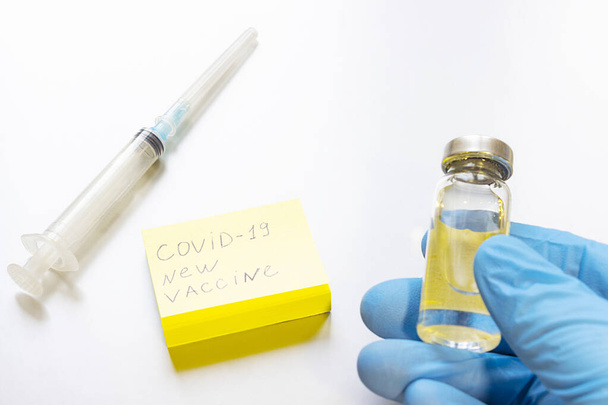 The syringe and the coronavirus vaccine are on the table. the concept of Free vaccination against coronavirus in the world in 2021. the inscription on the paper -  COVID-19 new vaccine. - Photo, Image