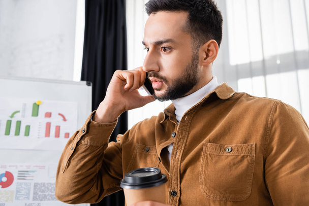 Muslimischer Geschäftsmann spricht auf Smartphone und hält Kaffee, um unscharf in den Vordergrund zu treten  - Foto, Bild