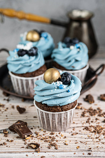 Several muffins or cupcakes with blue shaped cream and blueberrieson at white table. Rustic style copyspace. - Foto, Imagen