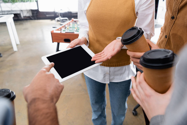 Καλλιεργημένη άποψη του επιχειρηματία δείχνοντας ψηφιακή ταμπλέτα κοντά σε συναδέλφους με καφέ για να πάει  - Φωτογραφία, εικόνα