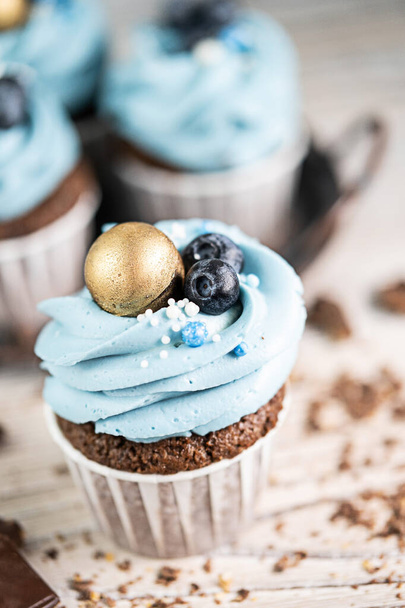 Several muffins or cupcakes with blue shaped cream and blueberrieson at white table. Rustic style copyspace. - Фото, изображение