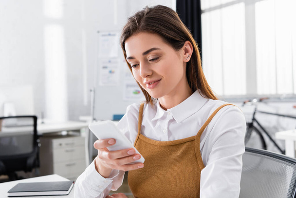 Positive businesswoman using smartphone in office  - Foto, imagen