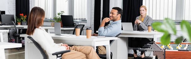 Multiethnic businesspeople talking near takeaway coffee and laptops in office, banner  - Fotó, kép