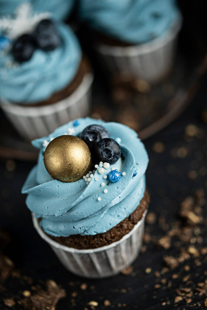 Several muffins or cupcakes with blue shaped cream and blueberrieson at black table. Rustic style copyspace. - Φωτογραφία, εικόνα