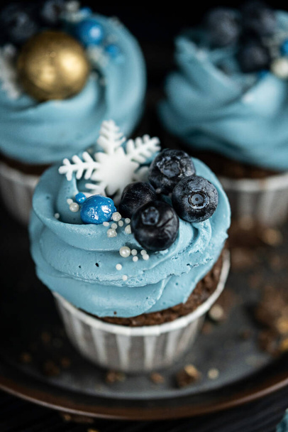 Several muffins or cupcakes with blue shaped cream and blueberrieson at black table. Rustic style copyspace. - Photo, Image