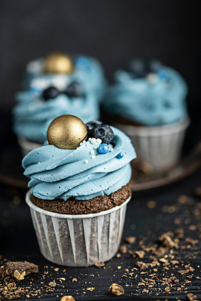 Several muffins or cupcakes with blue shaped cream and blueberrieson at black table. Rustic style copyspace. - Fotografie, Obrázek