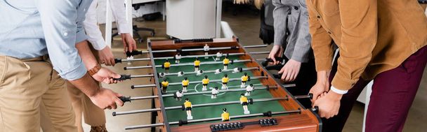 Обрезанный вид на бизнес-людей, играющих в настольный футбол в офисе, баннер  - Фото, изображение