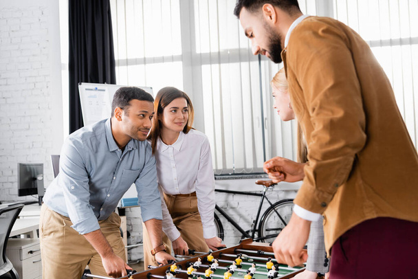 Multicultural business people looking at each other near table soccer in office  - Photo, Image
