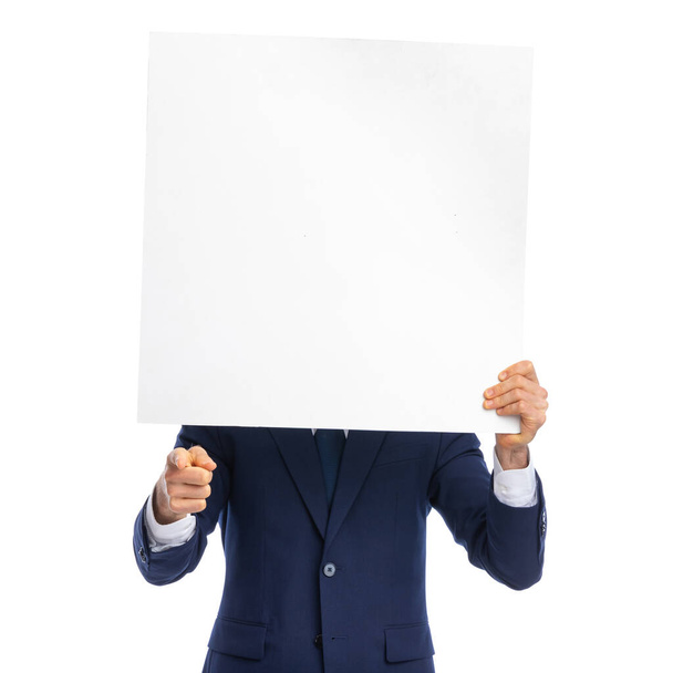 face covered man in elegant navy blue suit holding empty board and pointing finger, standing isolated on white background in studio - Fotoğraf, Görsel