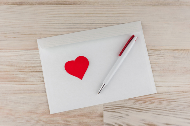 love mail: de witte lege enveloppe voor brieven, een witte balpen en een rood hart rust op een linnen doek - Foto, afbeelding
