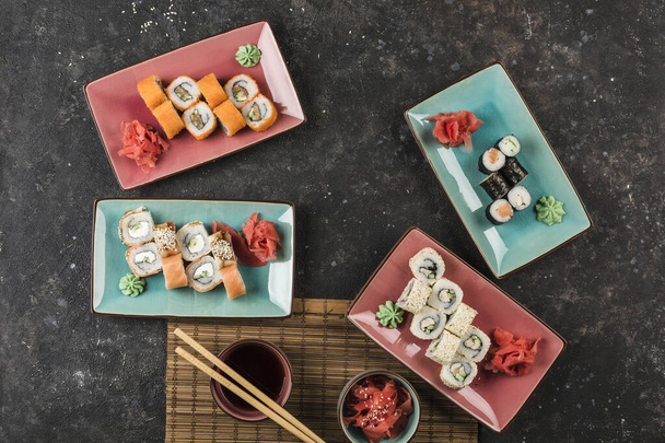 Αρκετά πιάτα σούσι ρολά σερβίρεται από τον σεφ σε ένα σκοτεινό φόντο. Άποψη από ψηλά με ένα αντίγραφο-χώρο. Φαγητό εστιατορίου. Επίπεδη - Φωτογραφία, εικόνα