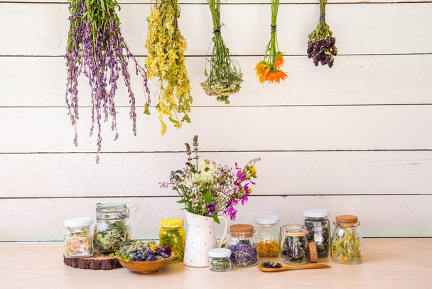 Lot of various herbal medicinal plants gathered and drying in room and dried herbs in glass jars on shelf. Herbalist concept. Fireweed, heal-all, woundwort, yarrow, cowslip, meadowsweet, pot marigold. - Photo, Image