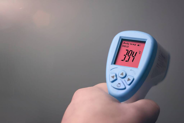 Nierozpoznawalna osoba trzymająca cyfrowe urządzenie do wykrywania temperatury ciała. Poziomy obraz z przestrzenią do kopiowania. - Zdjęcie, obraz