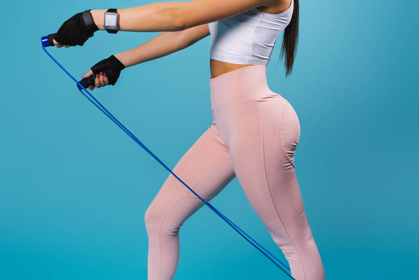 Silhouette of a young girl with pumped up buttocks in leggings with a skipping rope on a blue background. - Foto, imagen