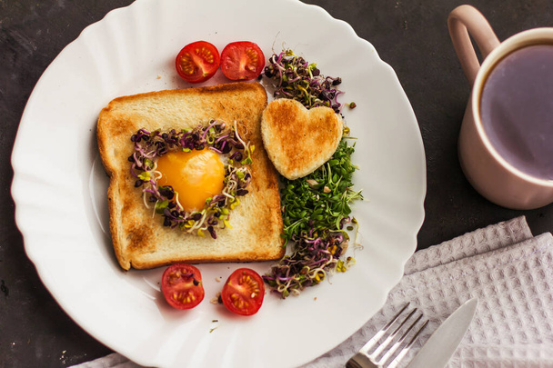 Egg in a hole of bread heart shape, microgreens, healthy food Breakfast, tea, black background - Photo, image