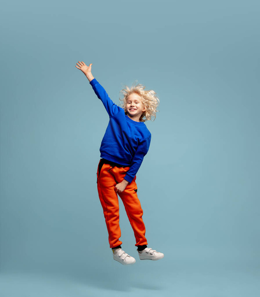 Happy curly boy isolated on blue studio background. Looks happy, cheerful, sincere. Copyspace. Childhood, education, emotions concept - Fotó, kép