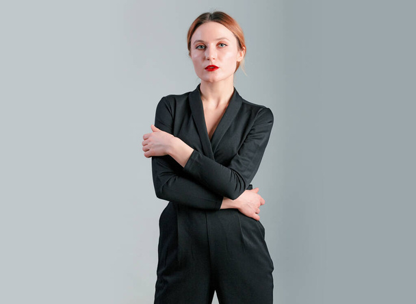Elegant business woman in black classic jumpsuit posing over gray background. - Photo, Image