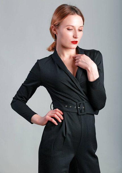 Elegant business woman in black classic jumpsuit posing over gray background. - Photo, image