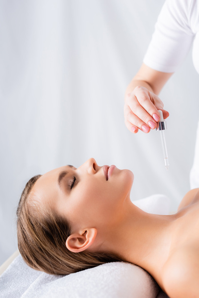 beautician holding pipette with serum near woman in spa salon  - Photo, Image