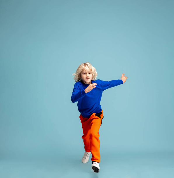 Happy curly boy isolated on blue studio background. Looks happy, cheerful, sincere. Copyspace. Childhood, education, emotions concept - Valokuva, kuva