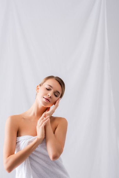 young woman wrapped in towel touching face on white - Foto, Bild