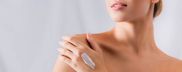 partial view of young woman with bare shoulders and cream on hand on white, banner - Foto, imagen