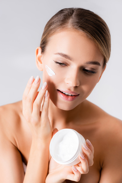young woman with bare shoulders holding jar and applying face cream isolated on white - Фото, изображение