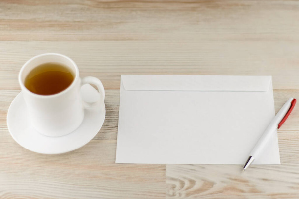 Ofiste sakin bir şekilde çalışmak - mektup yazmak ve göndermek için hazırlanmış bir zarf ve ferahlatıcı yeşil çay ile beyaz kupa da yakınlardadır - Fotoğraf, Görsel