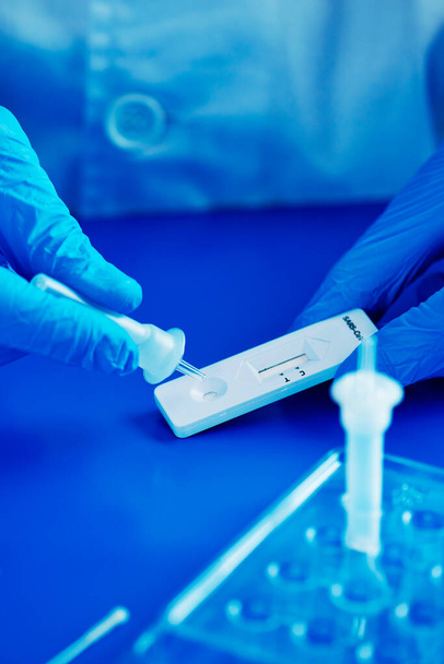 gros plan d'une personne, portant des gants chirurgicaux bleus, plaçant l'échantillon dans le dispositif de diagnostic de l'antigène covid-19, sur une surface bleue - Photo, image