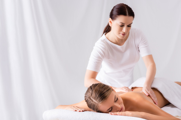brunette masseur massaging back of woman on massage table in spa salon - Foto, Imagen