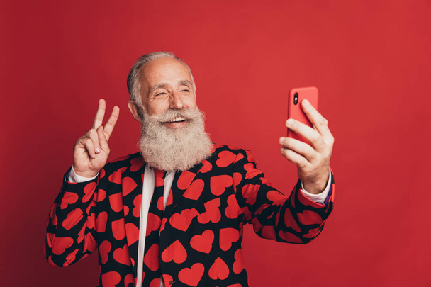 Photo of old gentleman hold telephone take selfie show v-sign wear heart print tuxedo tie isolated red background - Φωτογραφία, εικόνα