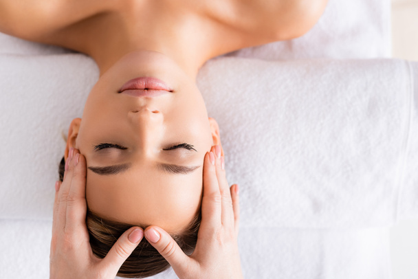 top view of masseur doing facial massage to woman in spa salon  - Zdjęcie, obraz