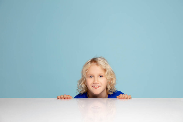 Happy curly boy isolated on blue studio background. Looks happy, cheerful, sincere. Copyspace. Childhood, education, emotions concept - Foto, Imagem