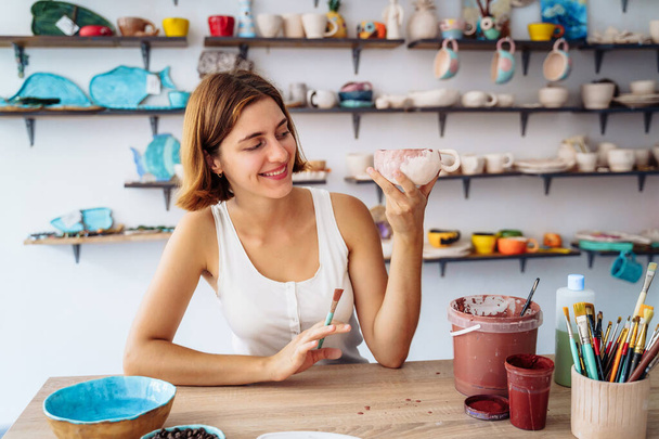 Potter regardant une tasse faite main, produite dans son propre atelier. Femme examinant l'argile itmes à vendre. Vérifier méticuleusement les défauts, admirer tasse d'argile. - Photo, image