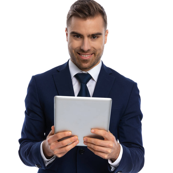 ritratto di un uomo d'affari sorridente in tuta blu navy con pad, in piedi e in posa isolato su sfondo bianco in studio - Foto, immagini