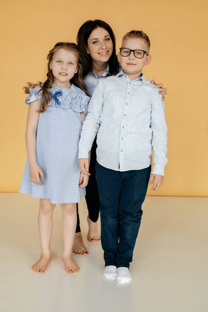 Mom and her children are in the room on a yellow background hugging each other. Love and care concept. Helping children with special needs. Mothers Day. - Foto, Imagem