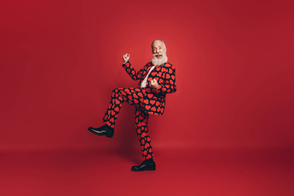Photo of excited gentleman raise fists knee celebrate open mouth wear heart print tux shoes isolated red background - 写真・画像