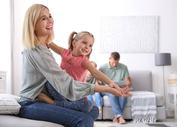 Happy mother playing with her daughter while father and son using laptop at home - Фото, изображение