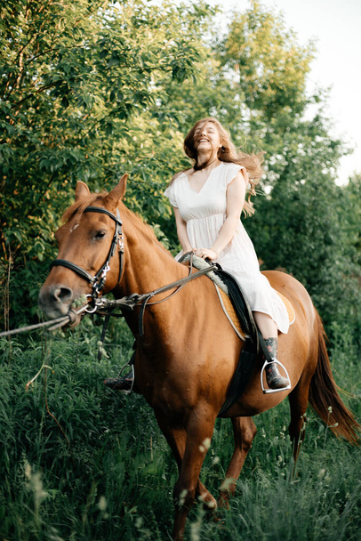 A girl rides a horse on a beautiful summer day. Long mane. In the background there is a forest. Pet care concept. - Foto, afbeelding