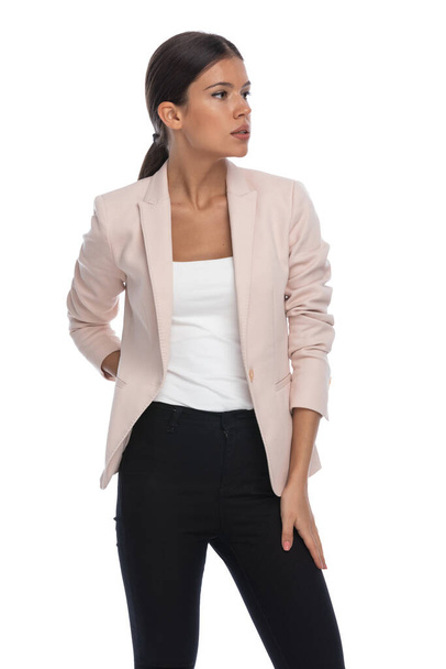 fiduciosa giovane donna d'affari in giacca rosa che tiene la mano dietro, guardando a lato e posa isolata su sfondo bianco in studio, ritratto - Foto, immagini